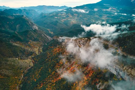 Téléchargez les photos : Une vue aérienne imprenable sur une vallée de montagne avec des nuages planant au-dessus, des arbres verts luxuriants et de la végétation couvrant le paysage, et la lumière du soleil regardant à travers l'atmosphère - en image libre de droit