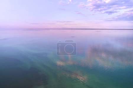 Téléchargez les photos : Un paysage naturel pittoresque avec un grand plan d'eau reflétant le ciel violet au crépuscule, créant une atmosphère fascinante avec le coucher du soleil à l'horizon - en image libre de droit
