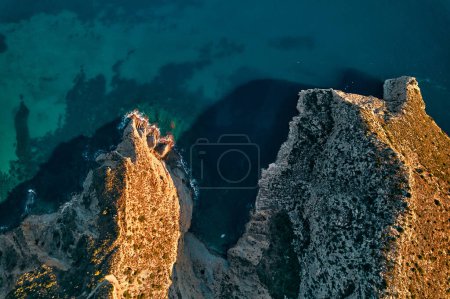 Téléchargez les photos : Une falaise avec une vue aérienne imprenable sur l'océan azur en contrebas, mettant en valeur un phénomène géologique majestueux fusionnant avec un paysage bleu électrique sous-marin - en image libre de droit