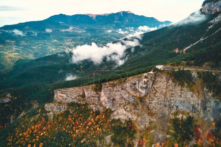 Téléchargez les photos : Une perspective aérienne d'une chaîne de montagnes montagneuses avec une végétation dense, des nuages éparpillés dans le ciel, se prélassant au soleil comme phénomène atmosphérique crée un paysage naturel captivant - en image libre de droit