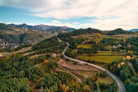 Téléchargez les photos : Une vue aérienne à couper le souffle d'une route sinueuse tissant à travers un terrain montagneux, entouré d'une verdure luxuriante et sous un ciel bleu clair - en image libre de droit