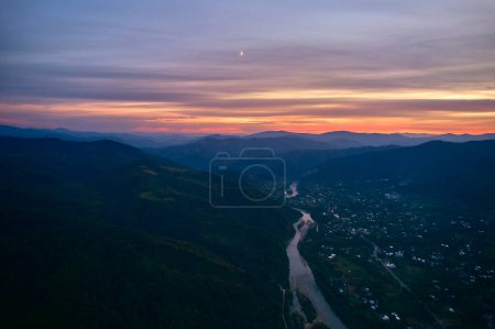Foto de Vista aérea desde un dron de una puesta de sol en las montañas con un río y un pueblo. Paisaje nocturno de un pueblo en las montañas. - Imagen libre de derechos