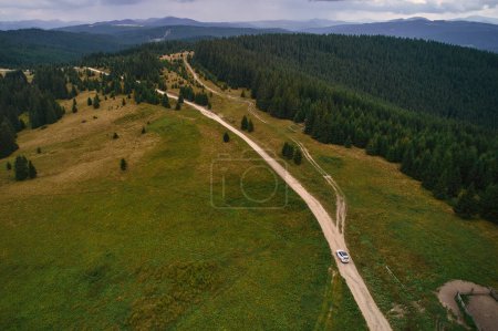 Foto de Vista aérea del dron de un coche que conduce a lo largo de una carretera a través de un bosque de montaña. Paisaje forestal sobre el telón de fondo de las montañas. - Imagen libre de derechos