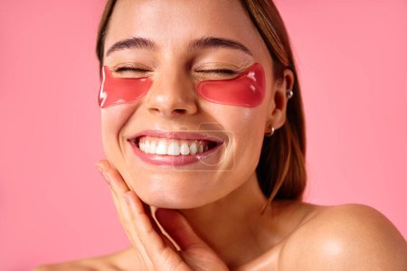 Téléchargez les photos : Belle femme avec des taches hydratantes sous ses yeux isolés sur fond rose. Soins du visage, cosmétologie, concept beauté. - en image libre de droit
