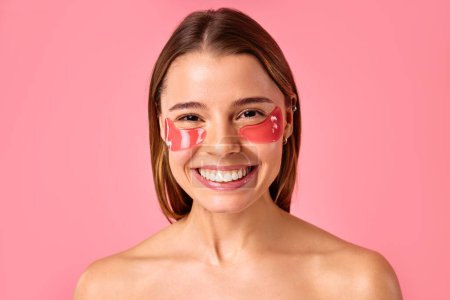 Téléchargez les photos : Belle femme avec des taches hydratantes sous ses yeux isolés sur fond rose. Soins du visage, cosmétologie, concept beauté. - en image libre de droit