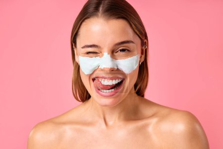 Téléchargez les photos : Belle femme heureuse utilisant un masque facial nettoyant pour les points noirs et les pores dilatés isolés sur fond rose. Soins de la peau, cosmétologie, concept beauté. - en image libre de droit
