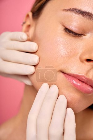 Während einer Hautbehandlung untersucht ein behandschuhter Fachmann das Gesicht, um einer Frau strahlende, gesunde Haut zu verleihen. Kosmetologie, Wellness und Hautpflege.