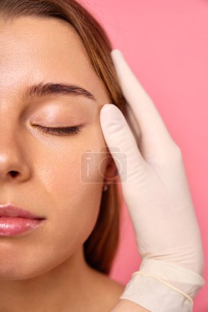 During a skin treatment, a gloved professional examines the face to give a woman radiant, healthy skin. Cosmetology, spa and skin care.