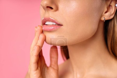 An elegant woman is portrayed up close, with radiant skin and touching her face gently against a pink backdrop. Ideal for discussions on beauty, skincare, and makeup