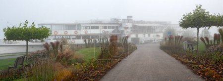 Photo for Excursion ship with paddle wheeler drive at foggy weather on the landing stage on the river Danube at Tulln, Austria - Royalty Free Image