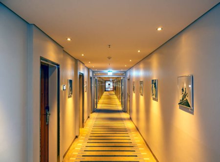 Foto de Vista a un largo pasillo del hotel con iluminación artificial e imágenes en las paredes - Imagen libre de derechos