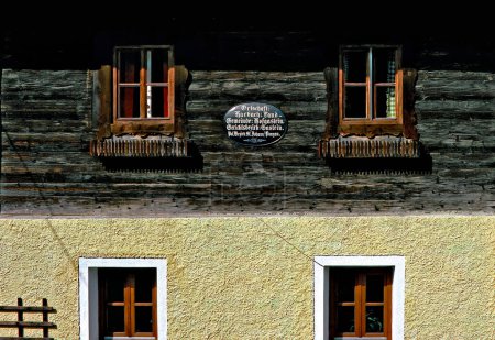 Photo for Facade of an old farm house with brick-built ground level and wooden upper floor. historic sheet metal sign with names of the administrative units in the community Hofgastein of Salzburg, Austria - Royalty Free Image