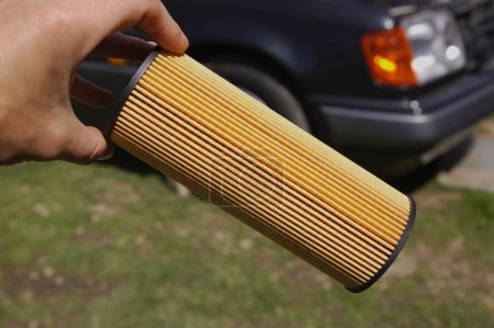 Foto de Human hand with new oil filter for car. Yellow oil vehicle filter with black car in the background. - Imagen libre de derechos