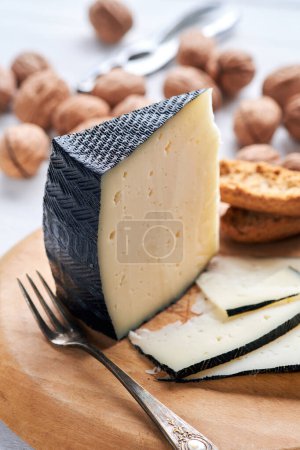 A wedge of cheese is displayed with crackers and walnuts on a cutting board.