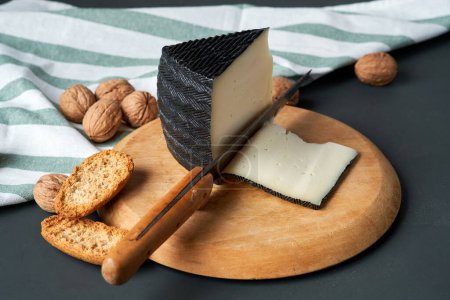 A wedge of artisan cheese with slices and whole walnuts on a rustic wooden board.