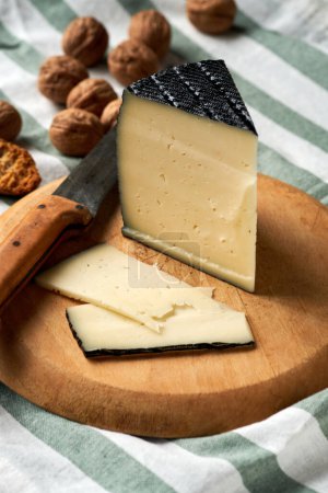 A wedge of artisan cheese with slices and whole walnuts on a rustic wooden board.