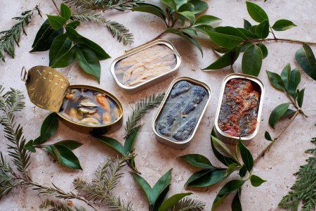 Assortment of canned seafood with green foliage on a stone surface