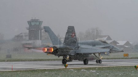 Photo for Meiringen Air Base Switzerland JANUARY, 18, 2013 Fighter jet take off with full afterburner under severe snow storm. Copy space. McDonnell Douglas F-18 Hornet of Swiss Air Force. - Royalty Free Image