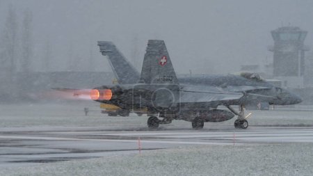 Photo for Meiringen Air Base Switzerland JANUARY, 18, 2013 Military airplane with the fire exiting from afterburner under a strong snowstorm. McDonnell Douglas F-18 Hornet of Swiss Air Force. Copy space. Modern - Royalty Free Image