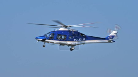 Photo for Blue Slovenian police helicopter patrolling the skies, clear blue background, detailed aircraft view. Copy Space. - Royalty Free Image