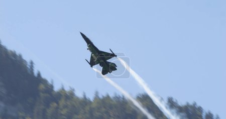 Téléchargez les photos : Mollis Suisse 19 août 2023 : Avion de chasse à Sunny Alpine Valley Flight. Ciel bleu et sentiers de fumée. Espace de copie. Général Dynamics F-16 Faucon combattant de l'armée de l'air belge Viper Demo - en image libre de droit