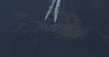 Photo for Mollis Switzerland August 19 2023: Fighter Jet in Sunny Alpine Valley Flight. Blue Sky and Smoke Trails. Copy Space. General Dynamics F-16 Fighting Falcon of Belgian Air Force Viper Demo - Royalty Free Image