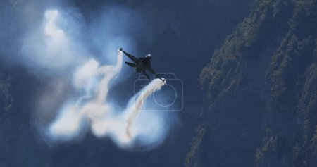 Photo for Mollis Switzerland August 19 2023: Fighter Jet in Sunny Alpine Valley Flight. Blue Sky and Smoke Trails. Copy Space. General Dynamics F-16 Fighting Falcon of Belgian Air Force Viper Demo - Royalty Free Image