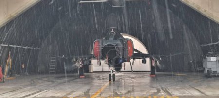 Photo for Combat aircraft parked inside an armored shelter, poised for takeoff to defend NATO skies, even on a day of heavy rain. Readiness and resilience. F-4 Phantom of Turkish Air Force. Copy Space. - Royalty Free Image