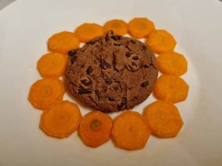 Köstliche Schokoladenkekse umgeben von dünnen Karottenscheiben auf einem weißen Teller