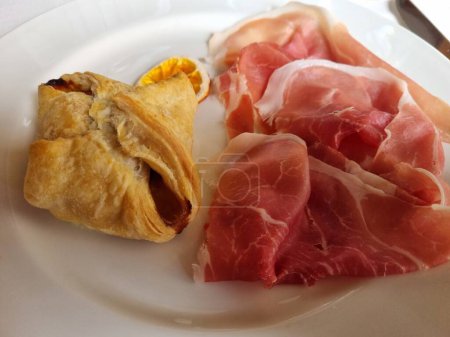 Close-up view of a gourmet appetizer featuring delicate prosciutto slices and a golden pastry