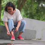 Asian woman sitting alone in the park, fixing her shoe lace, after a long walk