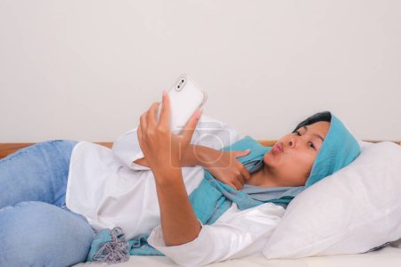 Téléchargez les photos : Indonésien fille couché sur le canapé prendre selfie photo avec smartphone - en image libre de droit