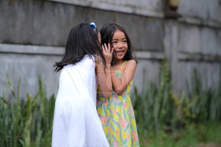 Téléchargez les photos : Deux petites filles asiatiques jouant chuchoter jeu en dehors de la maison - en image libre de droit