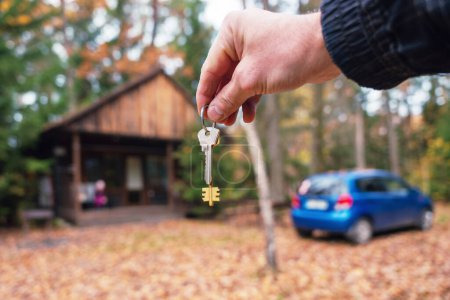 Photo for A man holds the keys to the house in his hands against the background of a residential country house and a car. The concept of buying and renting apartments. - Royalty Free Image