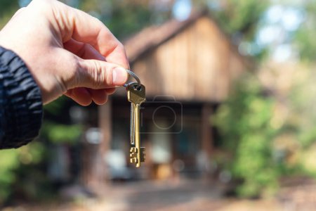 Photo for A man holds the keys to the house in his hands against the backdrop of a residential country house. The concept of buying and renting apartments. - Royalty Free Image