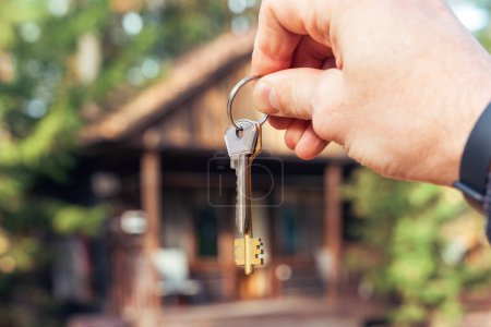 Photo for A man holds the keys to the house in his hands against the backdrop of a residential country house. The concept of buying and renting apartments. - Royalty Free Image