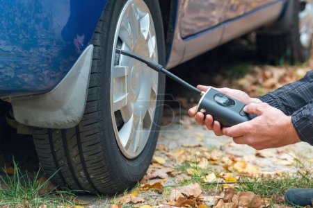 Photo for Inflating car tires with a portable wireless air pump outdoor. - Royalty Free Image