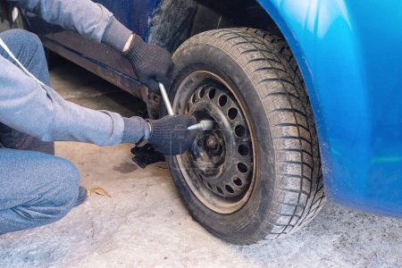 Un hombre desenrosca una rueda de coche en un garaje. Sustitución de ruedas de coche.
