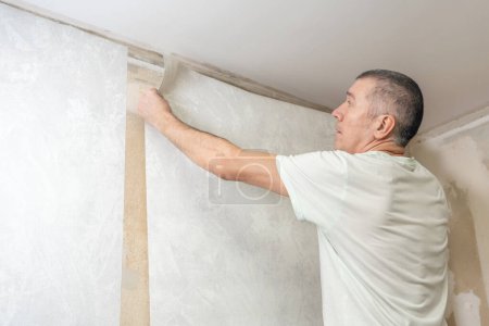 Photo for A man is gluing non-woven wallpaper on the wall. Room renovation. - Royalty Free Image