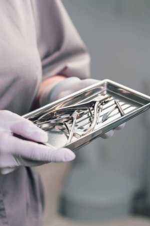 A girl in gloves holds a tray with sterile medical instruments for pedicure.