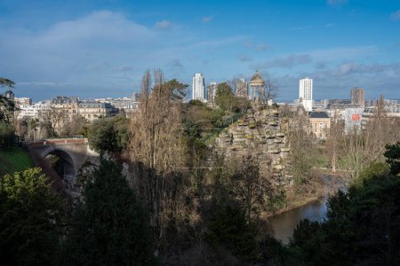 Foto de Park des Buttes Chaumont. Vista de la pasarela que une la isla Belvedere, el Templo del Sibyl y los edificios detrás - Imagen libre de derechos