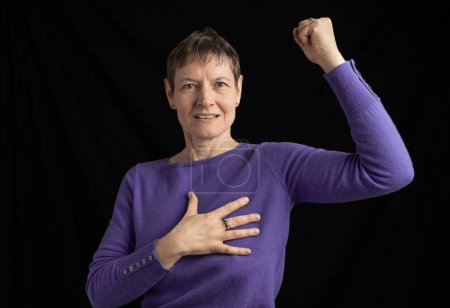 Photo for Studio shot of a woman with short hair wearing a purple sweater with cufflinks and with one hand on chest an one raised fist - Royalty Free Image