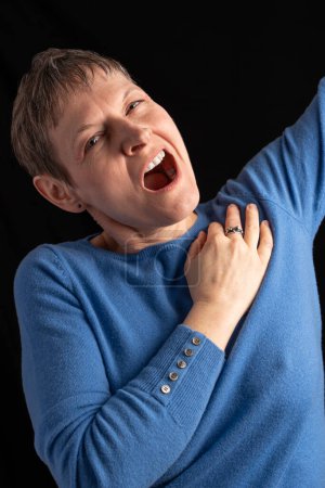 Photo for Studio shot of a woman with short hair wearing a purple sweater with cufflinks, yawns and with one hand on shoulder and stretches her arm - Royalty Free Image