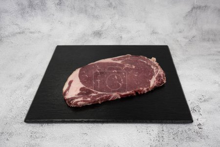 Photo for French culinary Still Life. Piece of beef rib loin placed on a black tile top. - Royalty Free Image