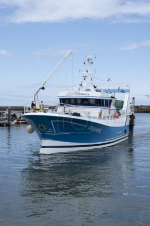 Foto de Port-en-Bessin-Huppain, Francia - 07 24 2023: Un barco pesquero azul entra en el puerto - Imagen libre de derechos