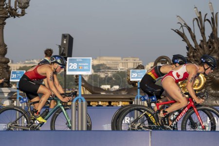 Foto de París, Francia - 08 17 2023: prueba de triatlón París 2024. Mujeres triatletas en la carrera ciclista en el puente Alexandre II - Imagen libre de derechos