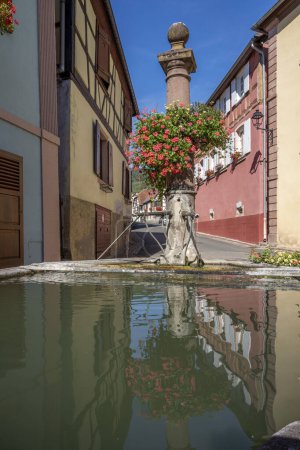 Téléchargez les photos : Hunawihr, France - 09 04 2023 : Vue d'une fontaine typique en pierre avec des fleurs colorées suspendues - en image libre de droit