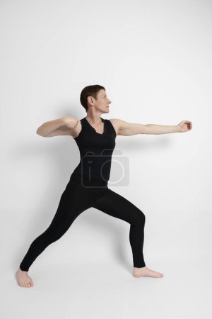 Photo for Athletic mature woman dressed in black, miming the sporty gesture of archery - Royalty Free Image