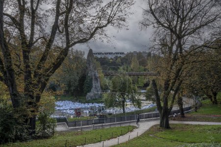 Foto de París, Francia - 11 11 2023: Park des Buttes Chaumont. Vista de la parte central del parque con pasarela, isla Belvedere, Templo del Sibyl y el lago en construcción debido a la renovación - Imagen libre de derechos