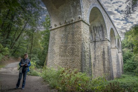 Vista de una mujer de pie y dibujando un puente ferroviario desde el fondo del bosque